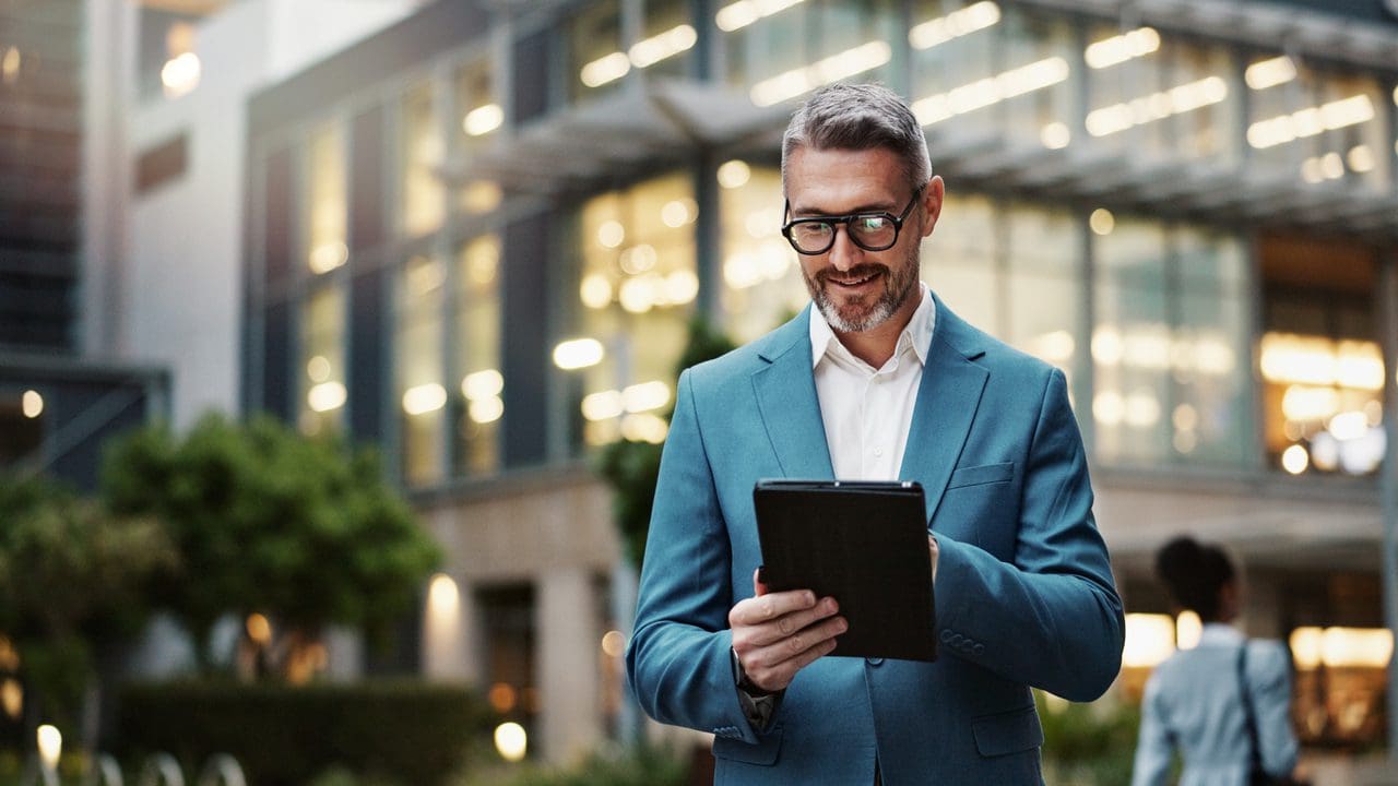 A man in a suit and glasses holding an ipad.