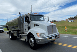 A white truck driving down the road near grass.