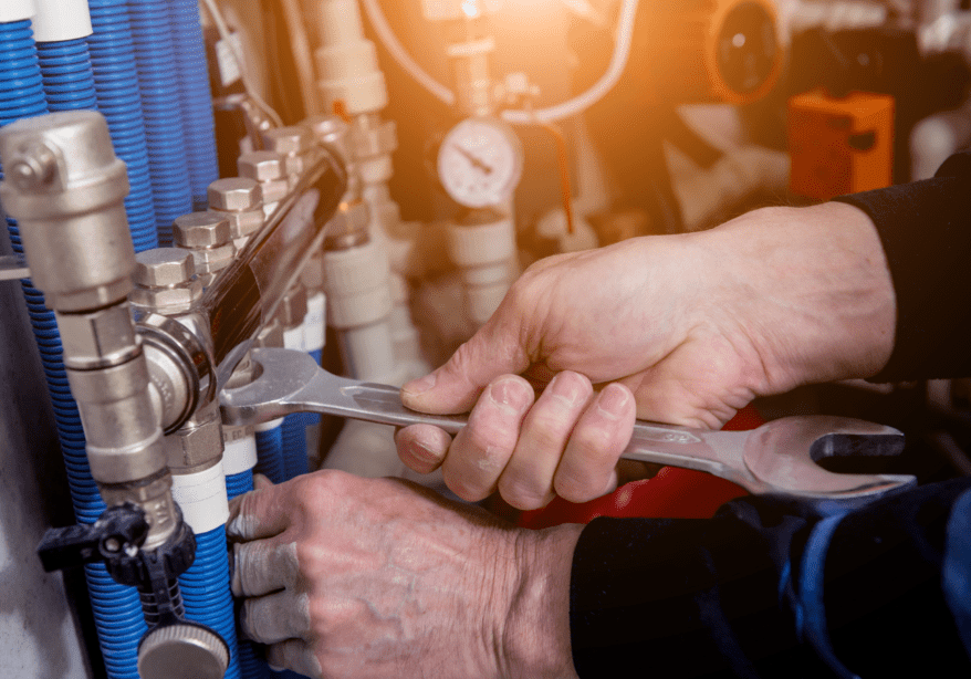 A person holding a wrench and adjusting the valves on an industrial machine.